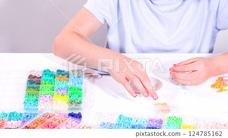 Delicate fingers of a young girl navigate through a treasure trove of bright, multicolored beads, each compartment revealing a new hue to choose from. 124785162