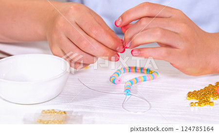 Delicate fingers of a young girl navigate through a treasure trove of bright, multicolored beads, each compartment revealing a new hue to choose from. She's immersed in the joyful task of stringing Delicate fingers of a young girl navigate through a treasure trove of bright, multicolored beads, each compartment revealing a new hue to choose from. She's immersed in the joyful task of stringing 124785164