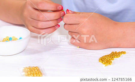 Delicate fingers of a young girl navigate through a treasure trove of bright, multicolored beads, each compartment revealing a new hue to choose from. She immersed in the joyful task of stringing 124785166
