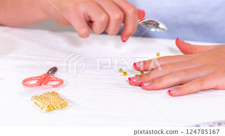 Delicate fingers of a young girl navigate through a treasure trove of bright, multicolored beads, each compartment revealing a new hue to choose from. She's immersed in the joyful task of stringing Delicate fingers of a young girl navigate through a treasure trove of bright, multicolored beads, each compartment revealing a new hue to choose from. She's immersed in the joyful task of stringing 124785167