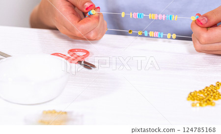 Delicate fingers of a young girl navigate through a treasure trove of bright, multicolored beads, each compartment revealing a new hue to choose from. She's immersed in the joyful task of stringing Delicate fingers of a young girl navigate through a treasure trove of bright, multicolored beads, each compartment revealing a new hue to choose from. She's immersed in the joyful task of stringing 124785168