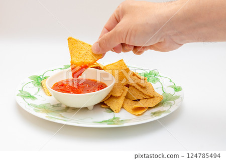 Tortilla chips and salsa sauce - Holding chips in hand and dipping them in salsa sauce 124785494