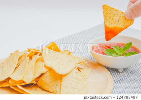 Tortilla chips and salsa sauce - Holding chips in hand and dipping them in salsa sauce 124785497