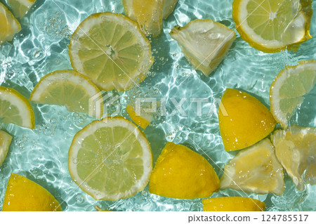 Refreshing turquoise citrus background with floating yellow lemon pieces Refreshing turquoise citrus background with floating yellow lemon pieces 124785517
