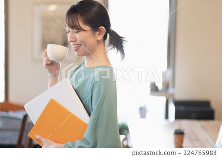 一名婦女站著喝咖啡，同時拿著筆記型電腦 124785983