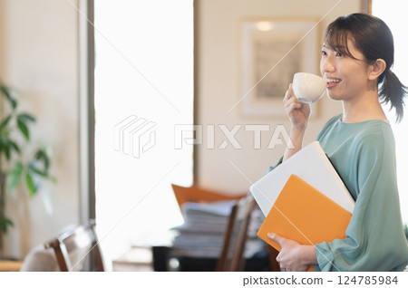 一名婦女站著喝咖啡，同時拿著筆記型電腦 124785984