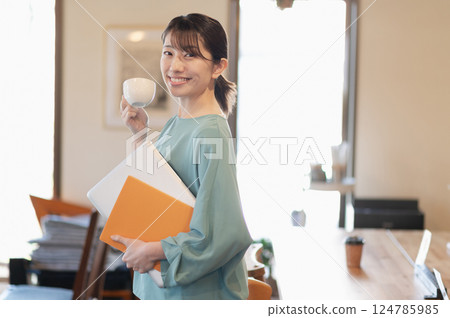 一名婦女站著喝咖啡，同時拿著筆記型電腦 124785985