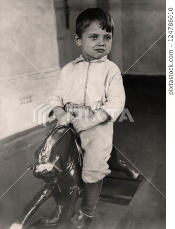 Vintage portrait of a little boy riding a wooden horse. Retro photo from 1932. 124786010