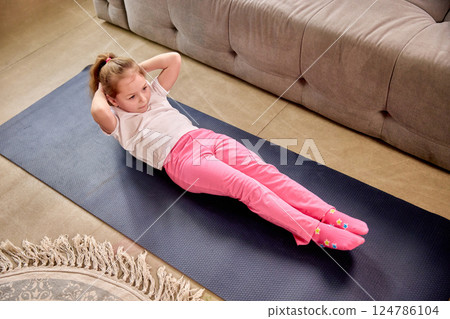 Focused child performing sit-ups on yoga mat during fun physical education class at home. Focused child performing sit-ups on yoga mat during fun physical education class at home. 124786104