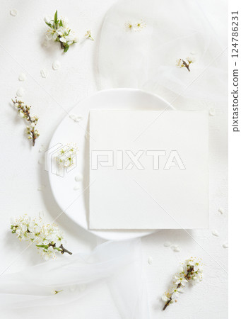 Blank card on plate near tulle and wild plums white flowers top view, romantic wedding mockup 124786231