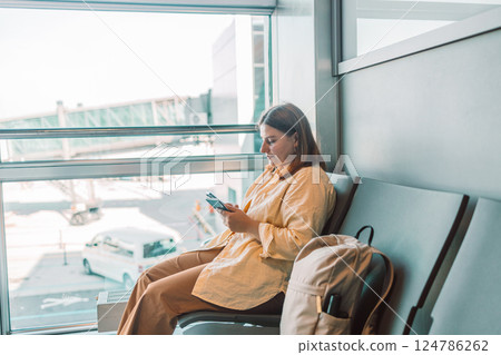 Young woman in the airport terminal using smartphones while waiting for her flight. 124786262