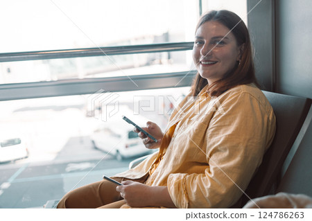 Young woman in the airport terminal using smartphones while waiting for her flight. Young woman in the airport terminal using smartphones while waiting for her flight. 124786263