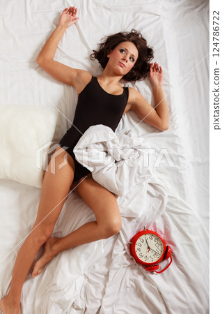 Sexy lazy girl lying with red alarm clock on bed 124786722