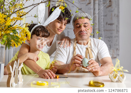 Father making handmade Easter egg wire decor with his sons at a festive spring table. DIY wire ornaments. 124786871