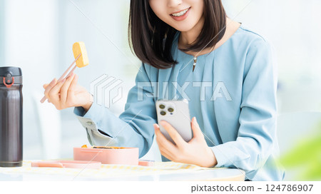 A woman/businesswoman eating lunch while looking at her smartphone A woman/businesswoman eating lunch while looking at her smartphone 124786907