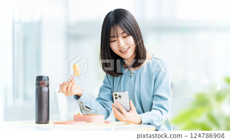 A woman/businesswoman eating lunch while looking at her smartphone A woman/businesswoman eating lunch while looking at her smartphone 124786908