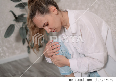 Young woman sitting discomfort in her injury knee pain while adjusting her a in posture cozy indoor setting 124786970