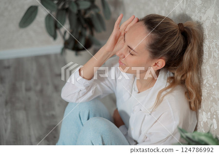 Young woman experiencing on migraine while sitting headache a couch in a modern living room home during daytime vertical photo 124786992