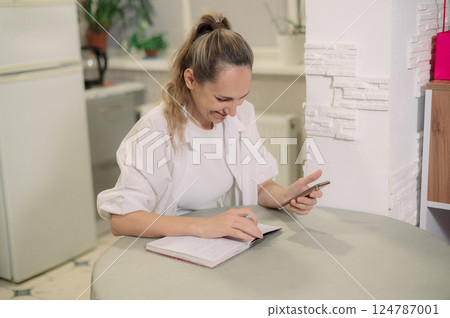 home up of a Close hands checking smart phone calendar and writing on agenda t at woman home up of a Close hands checking smart phone calendar and writing on agenda t at woman 124787001