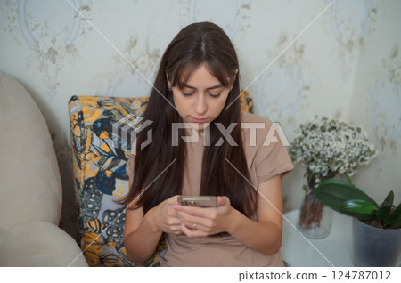 Young woman relaxing on cozy armchair, scrolling mobile smartphone screen during leisure time at home living room Young woman relaxing on cozy armchair, scrolling mobile smartphone screen during leisure time at home living room 124787012