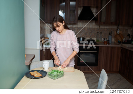 Woman slicing artisan cheese on wooden board, preparing fresh breakfast healthy food with crisp corn salad and whole wheat toast in sunlit kitchen 124787023