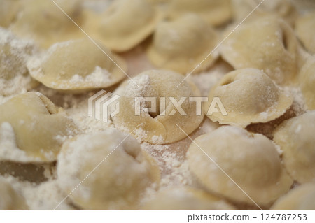 Close-up of traditional homemade dumplings sprinkled with flour, arranged on a kitchen surface ready for cooking. 124787253