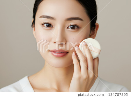 Young Japanese woman with natural skin holding a face powder puff (AI-generated image) 124787295