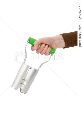 Hand holding a bulb planter tool with a green handle, isolated on white background. 124787632