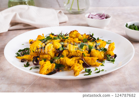 Baked small cauliflower steaks with onions and herbs on a plate on the table 124787682