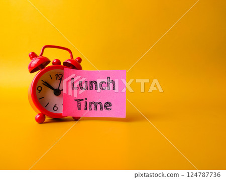 Red alarm clock with sticky note with the word Lunch Time on a yellow background. Red alarm clock with sticky note with the word Lunch Time on a yellow background. 124787736