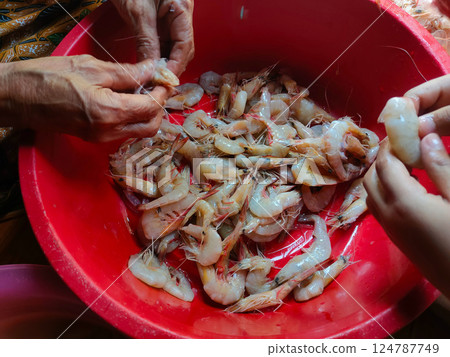 The shrimp in the red container are being peeled to be cooked. 124787749
