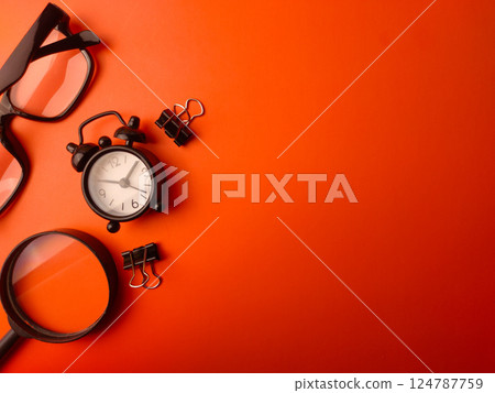 Top view magnifying glass,clock,paper clips and glasses on a orange background with copy space. Business concept. 124787759
