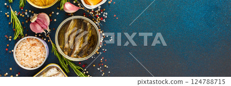 Different open tin cans with canned fish like salmon, mackerel, sprat, sardine, shrimp, among spices and herbs on a blue background, viewed from the top, banner Different open tin cans with canned fish like salmon, mackerel, sprat, sardine, shrimp, among spices and herbs on a blue background, viewed from the top, banner 124788715