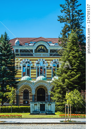 Holy Synod of the Bulgarian Orthodox Church in Sofia, Bulgaria. Bright church facade with trees, blue sky, domed entry, arched windows. Architecture reflect tradition, culture, religious faith Holy Synod of the Bulgarian Orthodox Church in Sofia, Bulgaria. Bright church facade with trees, blue sky, domed entry, arched windows. Architecture reflect tradition, culture, religious faith 124789137
