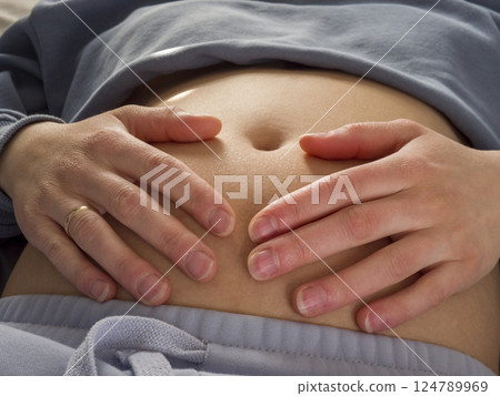 Expectant mother relaxing peacefully, gently touching swollen abdomen, expressing tender bond and quiet excitement during pregnancy journey 124789969