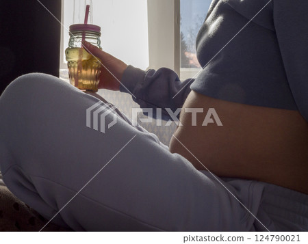 Pregnant woman relaxing indoors, sipping fresh juice, embodying wellness and nurturing her growing baby with mindful nutrition and calm 124790021
