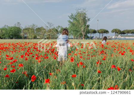 rear view of bigger child carrying on shoulders smaller one walking in a poppy field 124790661