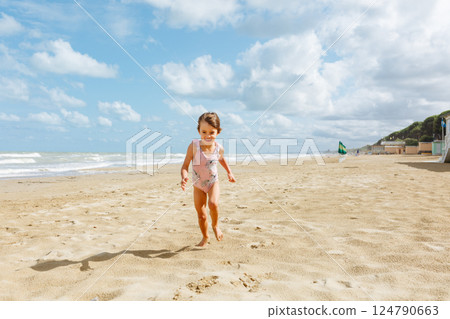 wide angle view of little happy girl in pink swimsuit running on the beach wide angle view of little happy girl in pink swimsuit running on the beach 124790663