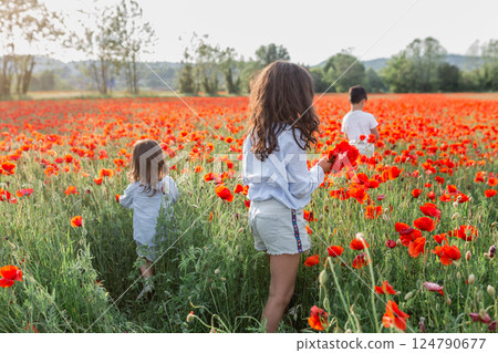 rear view of group of three children walking in a poppy field 124790677