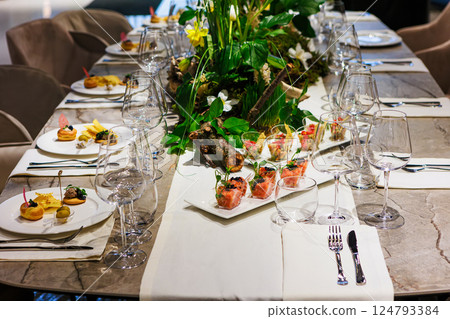 Luxurious dining table setup featuring gourmet appetizers, elegant glassware, floral centerpiece 124793384