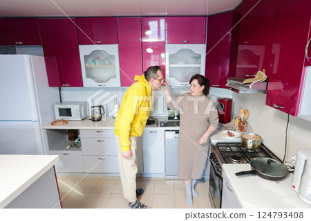 Woman feeds man with a gentle smile while he leans forward to taste food as they share lighthearted moment together during cooking in cozy kitchen space. Woman feeds man with a gentle smile while he leans forward to taste food as they share lighthearted moment together during cooking in cozy kitchen space. 124793408