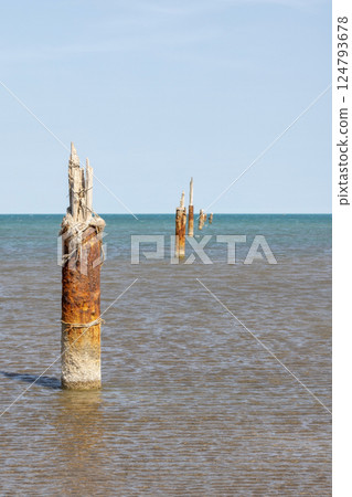 Weathered rusty posts rise from the shallow sea 124793678