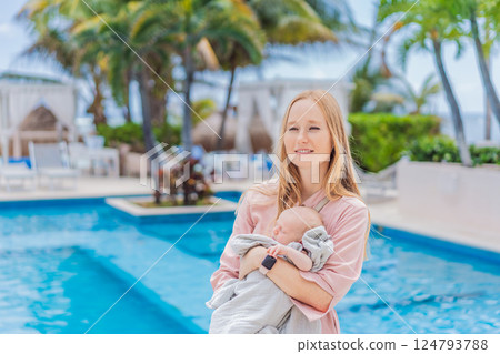 A mother holds her baby near a tropical pool, surrounded by lush greenery. This heartwarming moment captures family bonding, maternal love, and the serene beauty of a tropical getaway, perfect for A mother holds her baby near a tropical pool, surrounded by lush greenery. This heartwarming moment captures family bonding, maternal love, and the serene beauty of a tropical getaway, perfect for 124793788