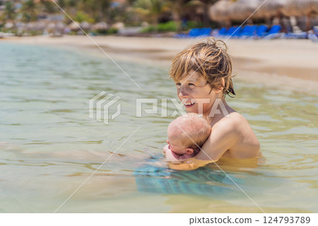 An older brother gently holds his baby sibling while swimming in the sea, sharing a joyful and heartwarming moment of family bonding and summer fun in the water. A perfect blend of love, care, and 124793789