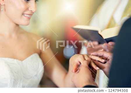 Wedding, marriage and putting ring on finger of bride in celebration of love, romance and commitment. Young couple getting married in church with groom giving jewellery to wife in wedding ceremony 124794308