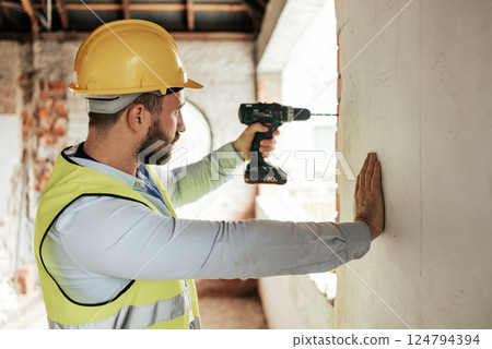 Construction worker, man or drilling wall with electric tool for utility lines, pipes or duct work in office building property. Engineering worker or architect drill on real estate construction site Construction worker, man or drilling wall with electric tool for utility lines, pipes or duct work in office building property. Engineering worker or architect drill on real estate construction site 124794394