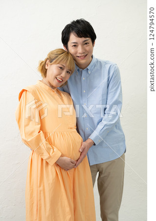 A husband holds his pregnant wife close to his stomach 124794570