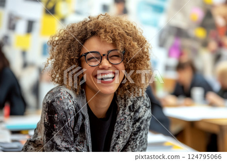 Smiling person with curly hair and glasses in a creative workspace, expressing joy. Concept of happiness, creativity, positivity. For enhancing work environment vibes. 124795066