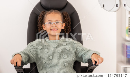Girl child, eye test glasses and smile in portrait at optometrist office, clinic or hospital for visual impairment. Young, female kid sitting or examination of eyes, sight and vision at optical exam 124795147