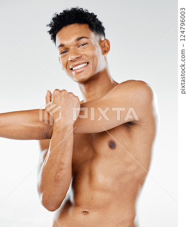 Portrait, fitness and man in studio stretching his shoulder and arms for a body exercise, training and workout. Smile, healthy and happy fitness model getting ready to start exercising with a warm up 124796003
